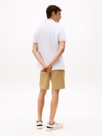 Witte polo, beige shorts en witte sneakers. De polo heeft korte mouwen en een klassieke kraag, terwijl de persoon zijwaarts staat.