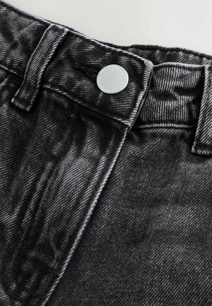 Nahaufnahme von schwarzem Denim-Stoff, der ein hochgeschnittenes Design mit einem silbernen Knopf und kontrastierenden Nähten am Bund zeigt.