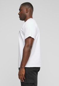 Hvid bomulds t-shirt med korte ærmer, rund hals og en afslappet pasform, vist fra en sidevinkel mod en grå baggrund.