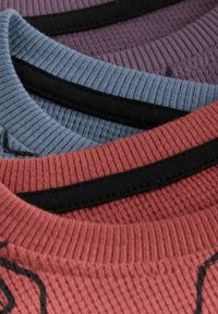 Three crew-neck sweaters stacked: maroon, blue, and purple colors. Each features ribbed texture and contrasting black neckline accents.