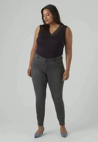 Body con encaje negro con detalles de encaje, combinado con jeans ajustados grises que presentan bolsillos y una textura suave, complementado con tacones azul claro.