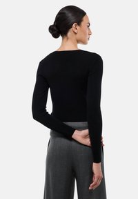 Pull en maille noir ajusté avec des manches longues et un décolleté bateau, associé à un pantalon gris. Texture lisse et design minimaliste.