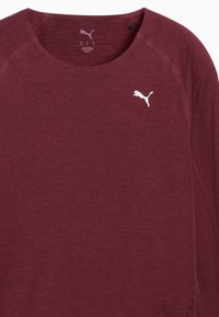 Burgundi spordisärk ümmarguse kaelusega, raglanvarrukatega ja valge Puma logo. Omab tekstuurset kangast ja väikeseid ventilatsioonidetaile ääres.