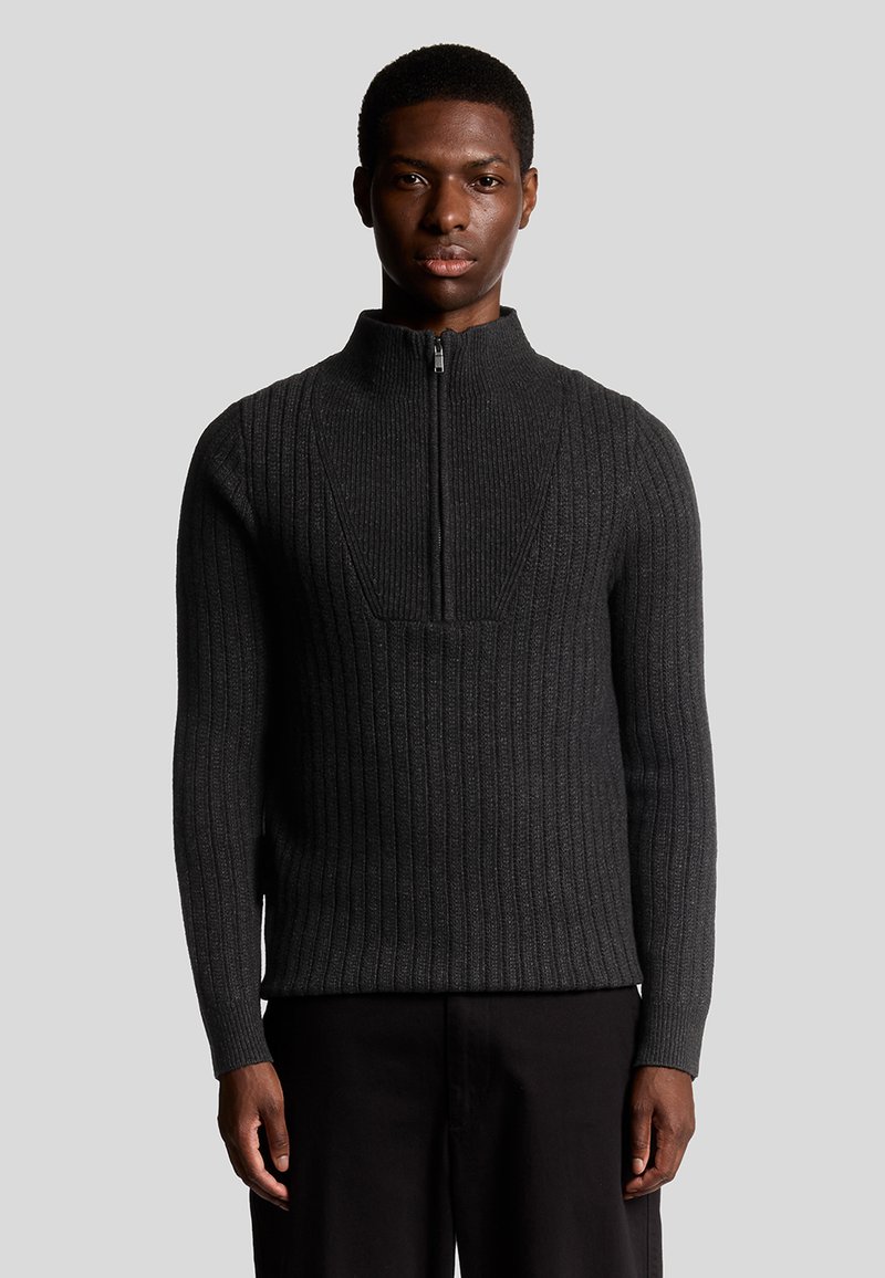 Donkergrijze geribbelde trui met een hoge kraag en een kwart ritssluiting. Heeft een gestructureerd patroon en een aansluitend ontwerp. Gemaakt van gebreid materiaal.
