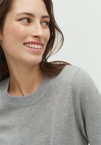 Pulover gri ușor, cu guler rotund cu nervuri și textură moale, având un design ajustat și cusături minime pentru un aspect curat.