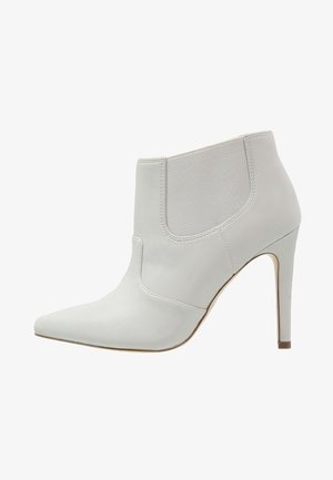 Valkoinen nahkainen nilkkuri, jossa on terävä kärki, sivujen elastinen paneli ja korkea stiletto-korko. Kenkä on varustettu sileällä pinnalla ja virtaviivaisella muotoilulla.