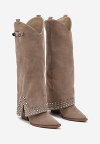Bottes en daim hautes jusqu'au genou couleur taupe avec des pointes, des clous en argent décoratifs le long de l'ourlet fendu, et un détail de boucle ajustable.
