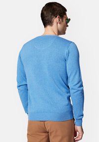 Niebieski sweter dziany z długimi rękawami, ściągaczami na mankietach i dole. Posiada klasyczny okrągły dekolt i gładką fakturę. Noszony na brązowych spodniach.
