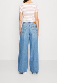 Bredde jeans i blå med høj talje, som har et klassisk fem-lomme-design og en lædermærkepatch bagpå. Sammen med en stribet crop top.