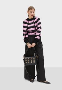 Maglione a righe rosa e nero con cappuccio, abbinato a pantaloni neri larghi. La borsa nera presenta dettagli quadrati dorati e una tracolla.