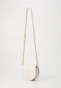 Piccola borsa a sella in pelle color crema con una lunga tracolla regolabile e chiusure metalliche dorate che pende su uno sfondo bianco.