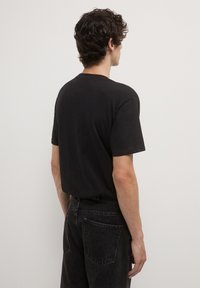 T-shirt in cotone nero con colletto tondo e maniche corte, mostrato da dietro. Abbinato a jeans scuri a vita alta.