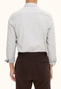 Maglietta grigia chiaro a maniche lunghe con una finitura testurizzata sottile. Polsini arrotolati e un design del giromanica dritto. Abbinata a pantaloni marroni.