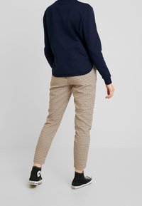 Navy sweatshirt med långa ärmar, tillsammans med beige och bruna rutiga tapered byxor och svarta högstövlar. Slät textur, avslappnad stil.