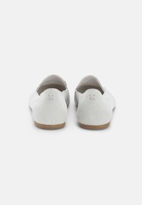 Scarpe slip-on in suede bianco con punta rotonda e suola in legno color tan. La parte posteriore presenta un semplice dettaglio a punto croce sul tallone.