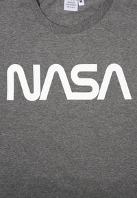 T-shirt in cotone grigio con un audace logo bianco "NASA", scollatura tonda e texture morbida. Etichetta di cura posizionata all'altezza del collo.