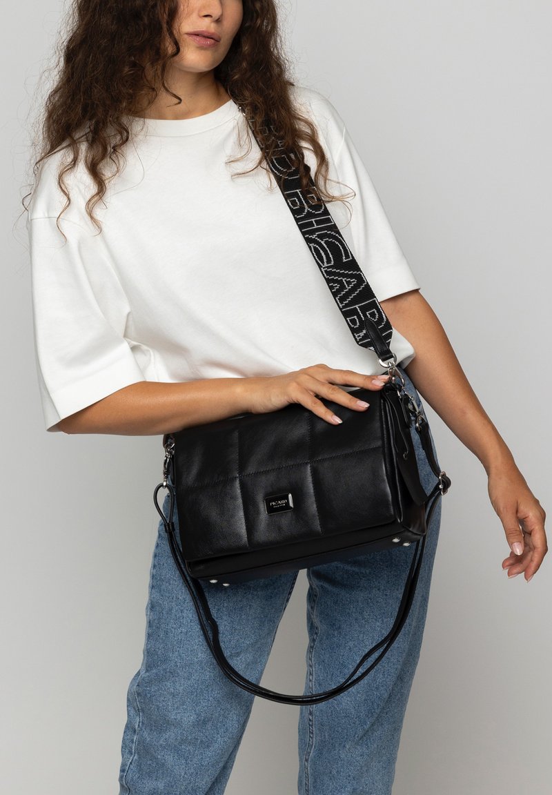 Schwarze Leder-Schultertasche mit einem gesteppten Design, ausgestattet mit einem kontrastierenden schwarz-weißen Tragegurt und silbernen Hardware-Akzenten.