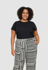 T-shirt nero a maniche corte abbinato a pantaloni a gamba larga con un audace motivo geometrico bianco e nero e tasche laterali.