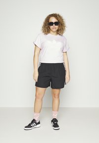 T-shirt viola a maniche corte con un logo bianco, pantaloni corti neri con strisce bianche, calze rosa e sneakers nere con suole bianche.