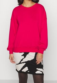 Fuchsia sweatshirt met lange mouwen, een ronde halslijn, een relaxte pasvorm en geribbelde manchetten, gecombineerd met een zwart-wit geblokte rok.