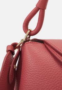 Czerwona skórzana torebka o teksturowanym wykończeniu, z złotym zapięciem i zakrzywionym uchwytem umożliwiającym łatwe noszenie. Wyrazisty detal w postaci przeszyć.