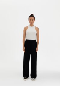 White ribbed sleeveless top paired with black wide-leg trousers and black sneakers, featuring a relaxed fit and elastic waistband.
