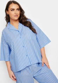 Ljusblå pyjamas med vertikala vita ränder, korta ärmar, krage med flik, knäppning framtill och bröstficka.