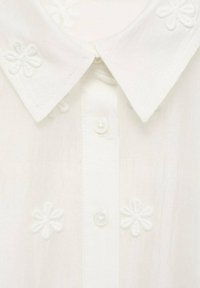 Vit skjorta med knappslutning, broderade blommor på kragen och tyget, med en slät textur och klassisk form.