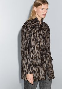 Cappotto con stampa animalier realizzato in un tessuto testurizzato con strisce nere e beige, chiusura a bottoni e due tasche anteriori.
