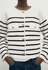 Gestreifter Cardigan in Weiß und Schwarz, mit einem runden Ausschnitt, silbernen Knöpfen und zwei vorderen Taschen mit Klappen. Weiches Material und lockere Passform.