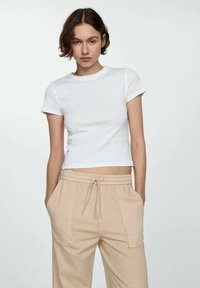 Witte katoenen crop t-shirt met korte mouwen, gecombineerd met beige joggingbroek met trekkoord, voorzien van voorzakken en een relaxte pasvorm.