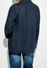 Námořnická lněná bunda s límečkem, dlouhými rukávy, bočními kapsami a rovný střih. Má texturovaný povrch a čistý vzhled.