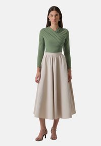 Green long-sleeve wrap top paired with a beige, high-waisted, full-length skirt. Skin-tone strappy heels. Smooth texture and minimalist design.