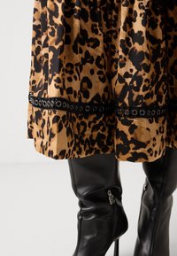 Jupe imprimé léopard avec bordure œillets noire associée à des bottes hautes en cuir noir avec des détails de fermeture éclair argentée.