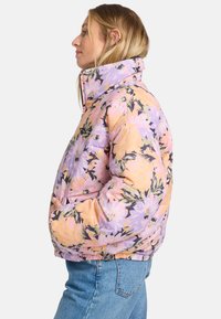 Jachetă puffer florală cu guler înalt. Prezintă modele de flori roz și violet pe un fond deschis. Manșete și tiv elastice.