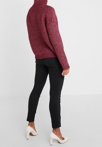 Donna che indossa un pullover a collo alto granata con texture, pantaloni neri aderenti e scarpe con tacco alto bianche, vista da dietro.