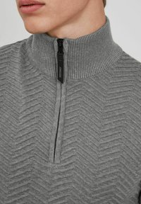 Sudadera gris con media cremallera, hecha de un tejido de punto texturizado, que presenta un cuello acanalado y un patrón en zigzag, con una cremallera negra y un detalle de etiqueta.