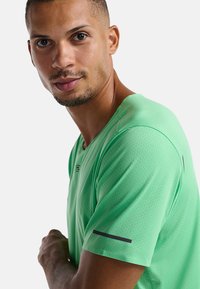 Camiseta atlética de manga corta verde, hecha de una tela texturizada y transpirable, con detalles en negro en las mangas y un diseño de cuello redondo.