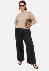 Hellbrauner, kurzärmeliger Pullover kombiniert mit hochgeschnittenen, weiten schwarzen Jeans. Accessoires mit einer Handtasche im Leopardenmuster und Sonnenbrille.