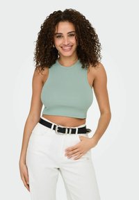 Muntgroene gepofte crop top met een hoge halslijn, gecombineerd met hoge witte jeans en een zwarte riem met een zilveren gesp.