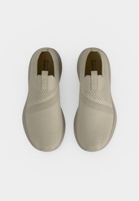 Paire de baskets beiges en maille sans lacets avec empeignes texturés et languettes, vues de dessus sur un fond blanc uni.