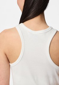 Top sin mangas blanco con texturizado acanalado que presenta un escote redondeado y amplias sisas, mostrando una textura suave y un diseño ajustado en la parte posterior.