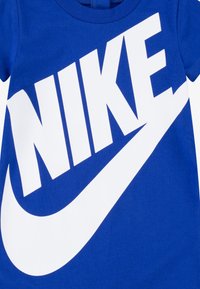 Blå bomulls-T-skjorte med en stor hvit "NIKE"-logo og swoosh-design. Kortermet med rund hals. Jevn tekstur.