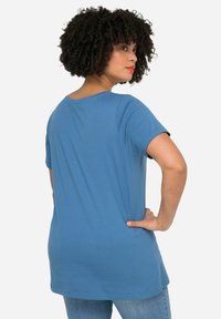 Camiseta de manga corta azul hecha de tela suave, con un escote redondeado y un corte relajado, combinada con jeans de mezclilla claros.