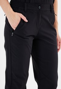 Sorte bukser lavet af letvægtsmateriale, med elastisk talje, sidelomme med lynlås og en skræddersyet pasform. Synlige sømdetaljer.