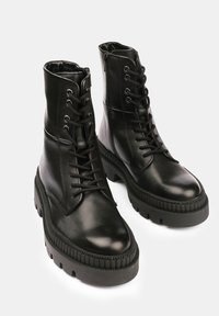 Botas de tobillo de cuero negro con punta redonda, cordones en la parte delantera y suela texturizada y duradera. Acabado mate elegante, con tacón grueso y cremalleras.