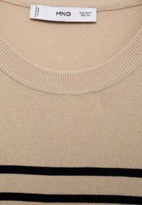 Beige svetr s žebrovaným kulatým výstřihem, se černými vodorovnými pruhy přes hrudník. Vyrobeno z měkkého pleteného materiálu.