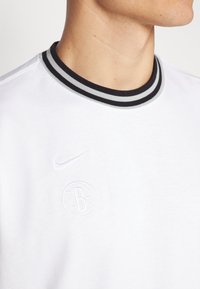 Hvit bomull T-skjorte med en svart og grå stripete rund hals, med en subtil Nike-logo og et preget basketballsymbol på brystet.