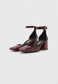 Pantofi din piele patent burgundy cu toc pătrat și curea pentru gleznă. Textură netedă cu talpă interioară căptușită și detalii cu logo auriu.