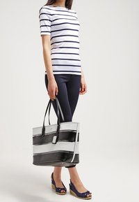 Svart- och vitrandig axelväska med dubbla handtag, tillverkad av texturerat material. Bärs med en marinblå topp och leggings, kompletterat med espadrillos.